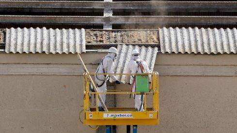 Dos trabajadores retiran placas de uralita con amianto en el tejado de una nave industrial de Arroyo de la Encomienda (Valladolid)