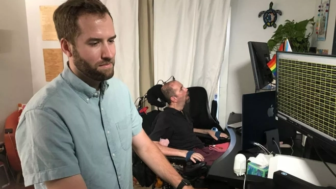 El becario postdoctoral y autor principal del estudio Nicholas Card prepara el sistema BCI junto a Casey Harrell El becario postdoctoral y autor principal del estudio Nicholas Card prepara el sistema BCI junto a Casey Harrell