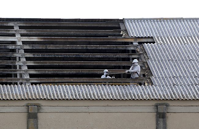 Dos trabajadores retiran placas de uralita con amianto en el tejado de una nave industrial de Arroyo de la Encomienda (Valladolid)