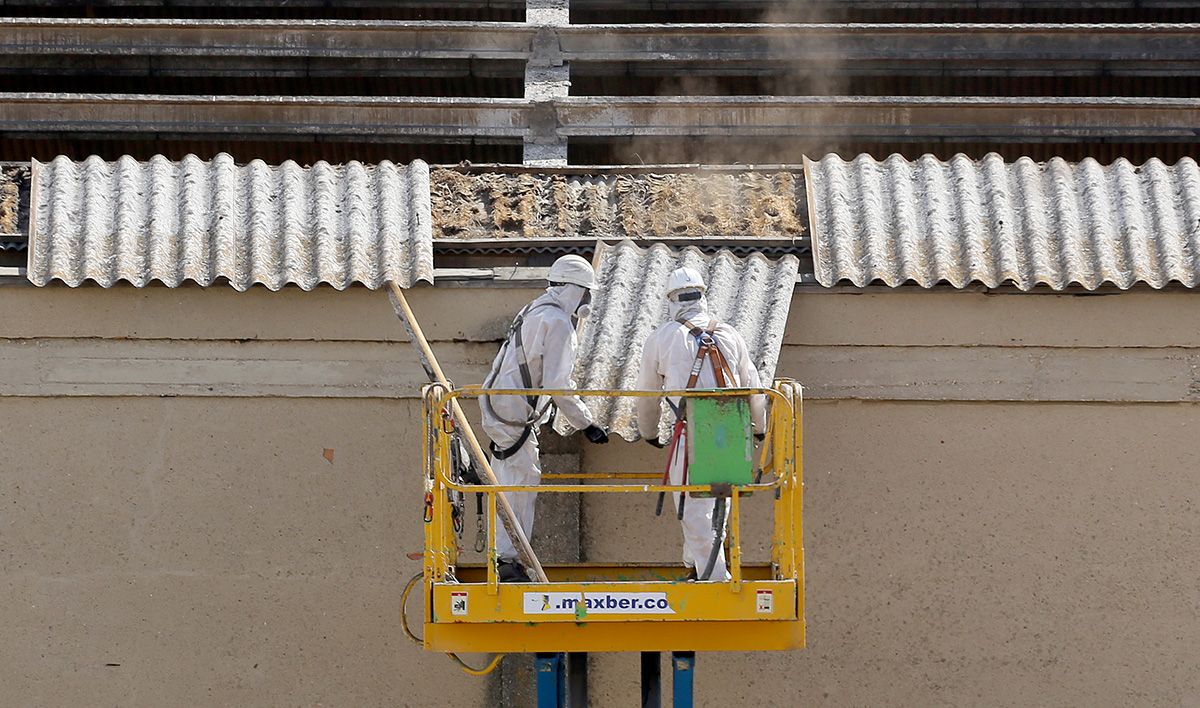 Dos trabajadores retiran placas de uralita con amianto en el tejado de una nave industrial de Arroyo de la Encomienda (Valladolid)